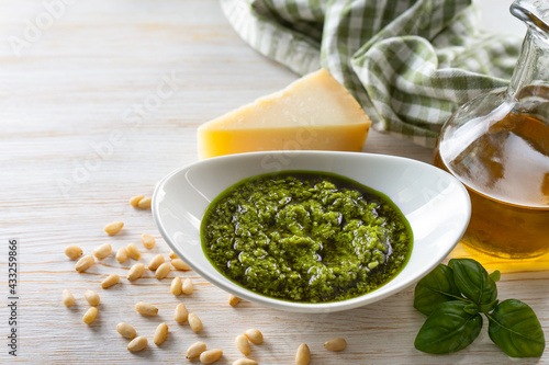Homemade pesto sauсe with ingredients. Sauсe pesto in white bowl with basil, olive oil, pine nuts and parmesan cheese on white wooden background with copy space for text.