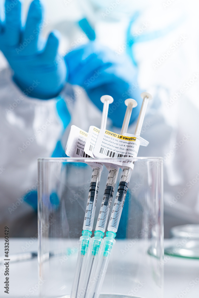 Focus on vaccine against Coronavirus COVID-19. Syringes label in the medical cup with antivirus on the medical worker table. Cure from respiratory syndrome strain of Corona virus. Ready to use shot. Focus on vaccine against Coronavirus COVID-19. Syringes label in the medical cup with antivirus on the medical worker table. Cure from respiratory syndrome strain of Corona virus. Ready to use shot.