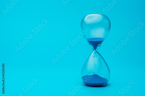 Hourglass with blue sand on blue background