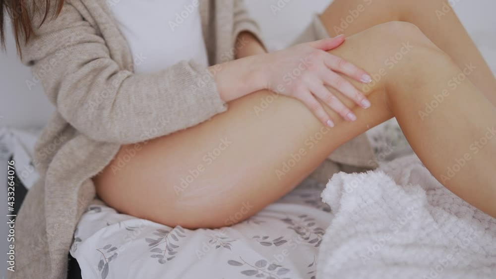 Crop woman sitting on bed and applying lotion on leg Crop woman sitting on bed and applying lotion on leg