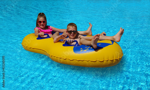 Boy and girl on inflatable float in outdoor swimming pool. © Alekss