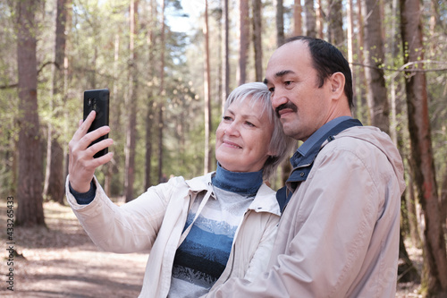Elderly interracial couple in a spring forest park, taking a selfie on your phone