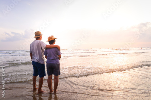An elderly Asian couple Stand together on the beach Look at the beautiful sea in the morning together. Travel concept to live happily in retirement age. copy space