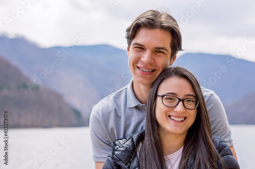 Smiling young couple standing near a lake looking to camera,close up.
