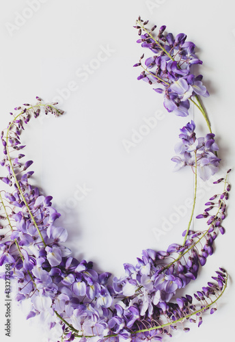 A white sheet of paper surrounded by twigs of blooming wisteria are on a white background. Copy space. View from the top point.
