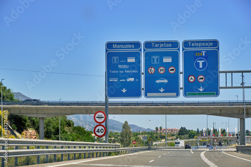 Light traffic in the toll plaza under the blue sky with multiple highway signs, electronic toll collection.