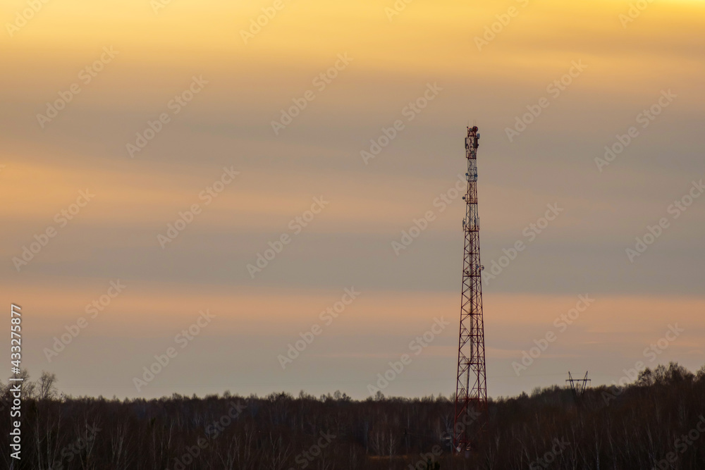 silhouette of a cell tower in the forest against the sunset sky