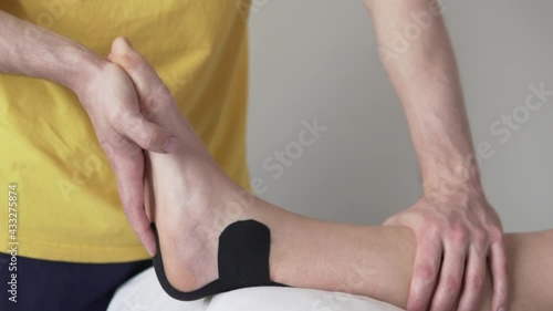 Stretching the Achilles tendon of an athlete after an injury, a rehabilitator does gymnastics for an ankle athlete in a tailpa, close-up. photo