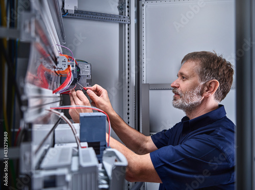 Male electrician examining power supply in electrical workshop photo
