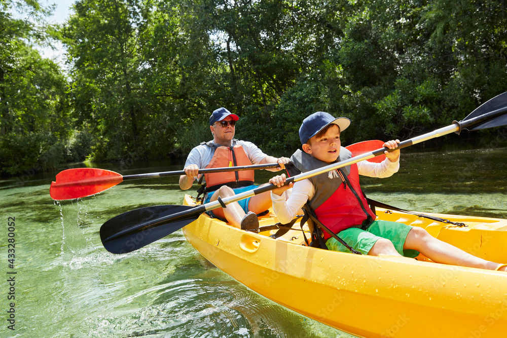 © Stefanie Aumiller/Westend61 - Boy with father in life jacket canoeing with oar in lake during picnic
