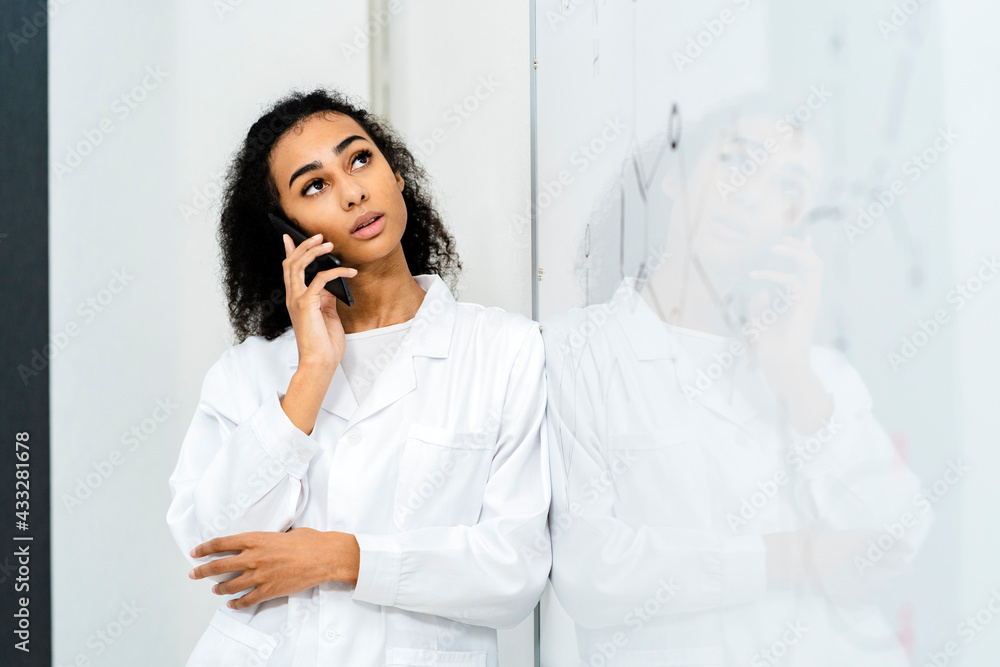 Young female doctor talking through smart phone while leaning on whiteboard in laboratory Young female doctor talking through smart phone while leaning on whiteboard in laboratory