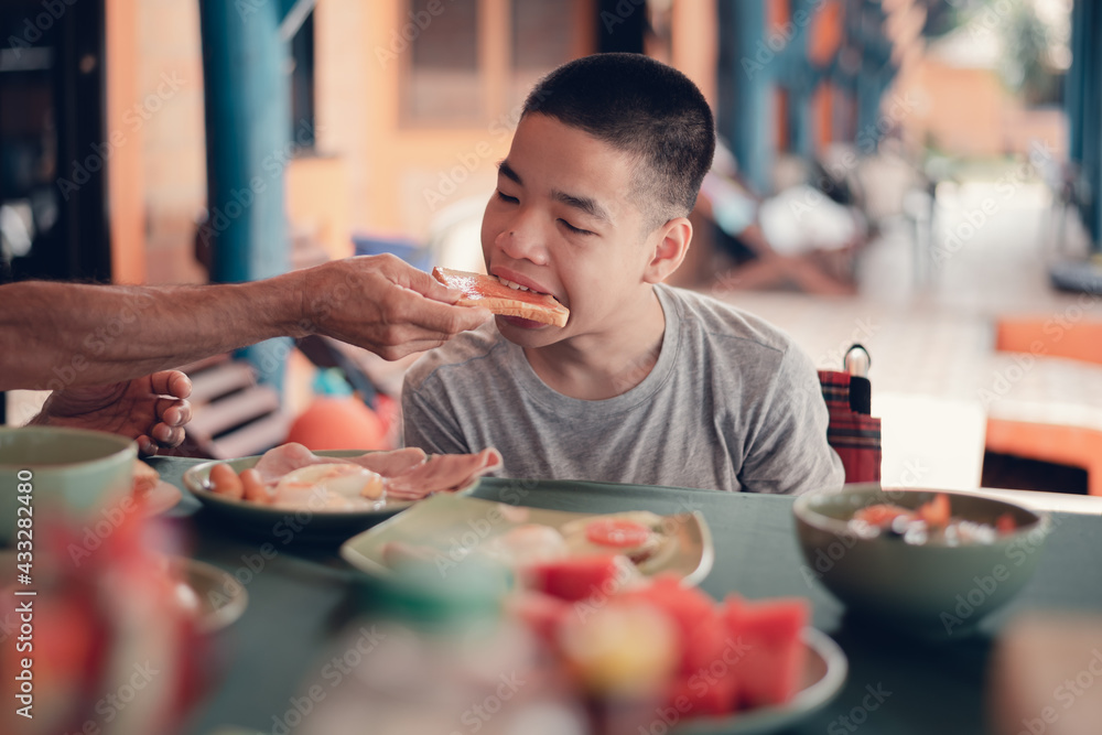 Father feeding food to Disabled child on the wheelchair in home or
