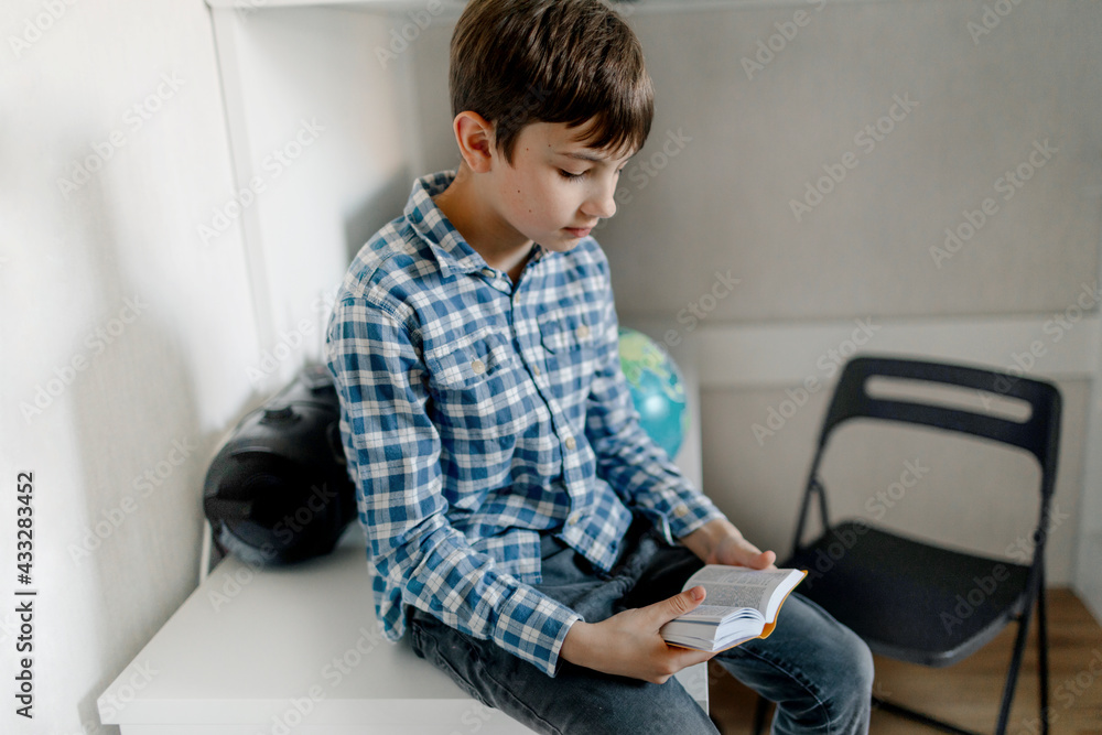 Boy reading dictionary while sitting on table at home Boy reading dictionary while sitting on table at home