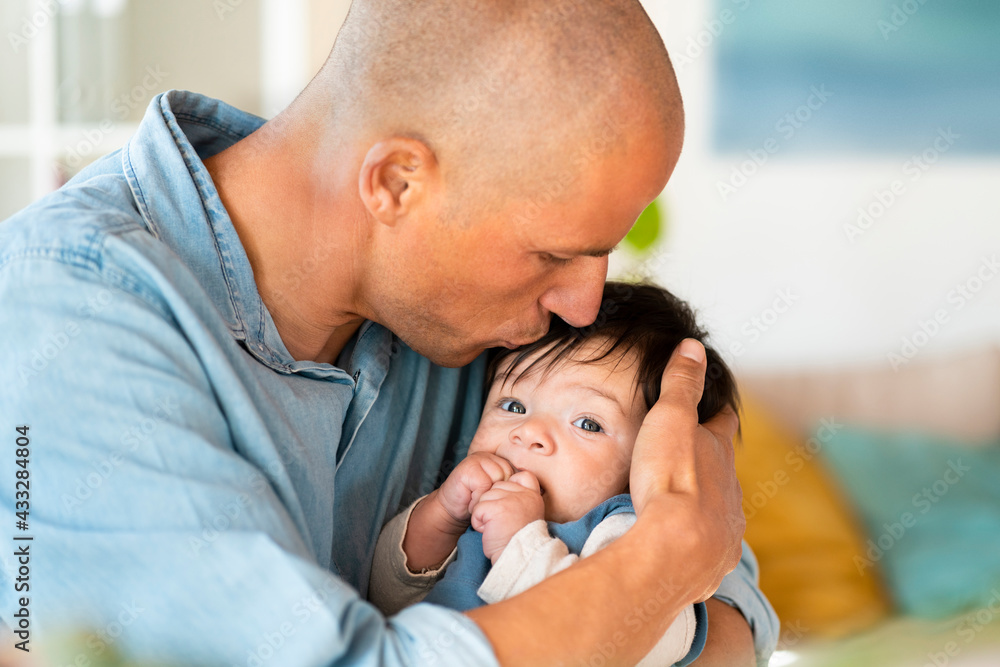 Mid adult father kissing his baby on forehead in living room Mid adult father kissing his baby on forehead in living room