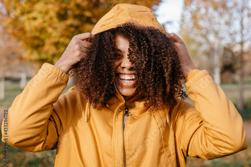 Cheerful Afro woman holding jacket hood in park during autumn  photo