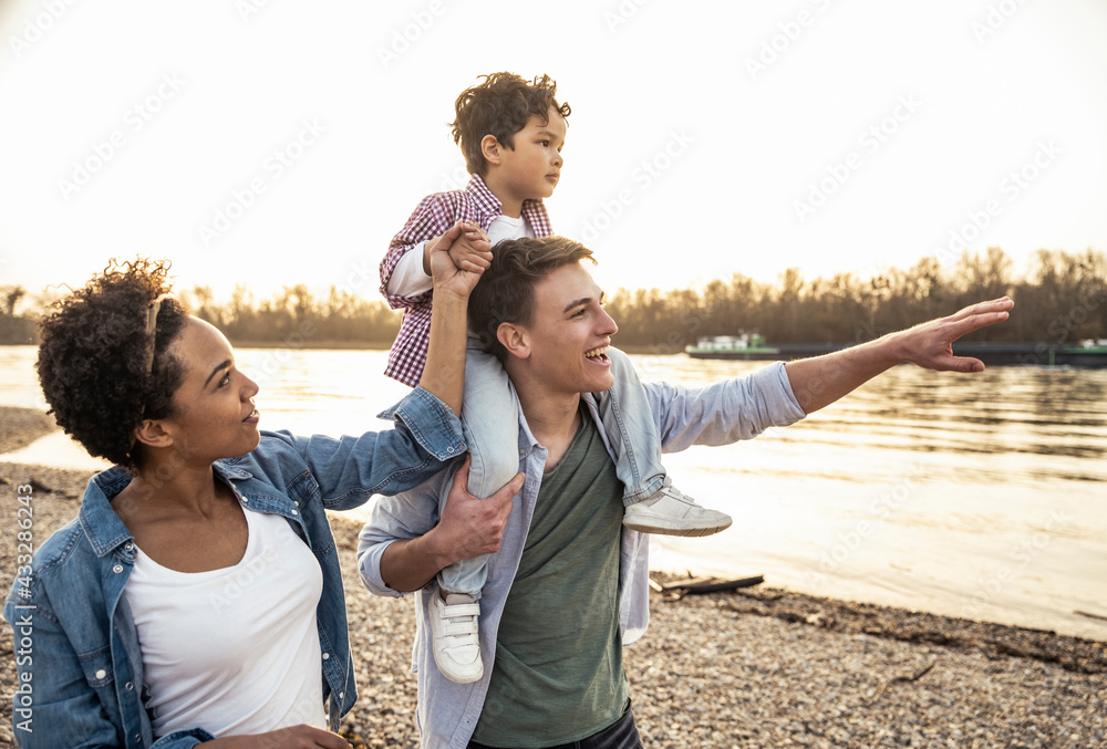 © Uwe Umst√§tter/Westend61 - Young man carrying boy on shoulders while standing by woman at lakeside