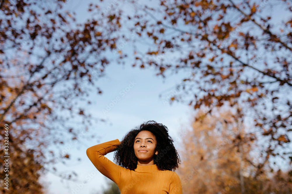 Thoughtful Afro woman with head in hand standing in park during autumn Thoughtful Afro woman with head in hand standing in park during autumn