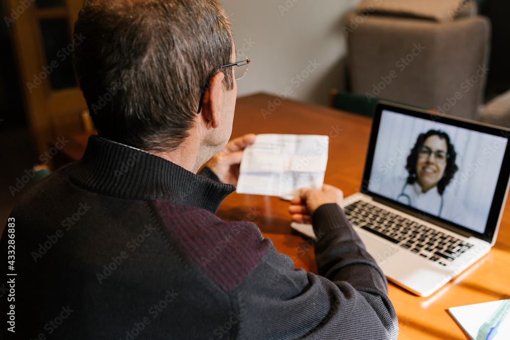 Senior male holding prescription while consultation on video call to female doctor at home during COVID-19 Senior male holding prescription while consultation on video call to female doctor at home during COVID-19