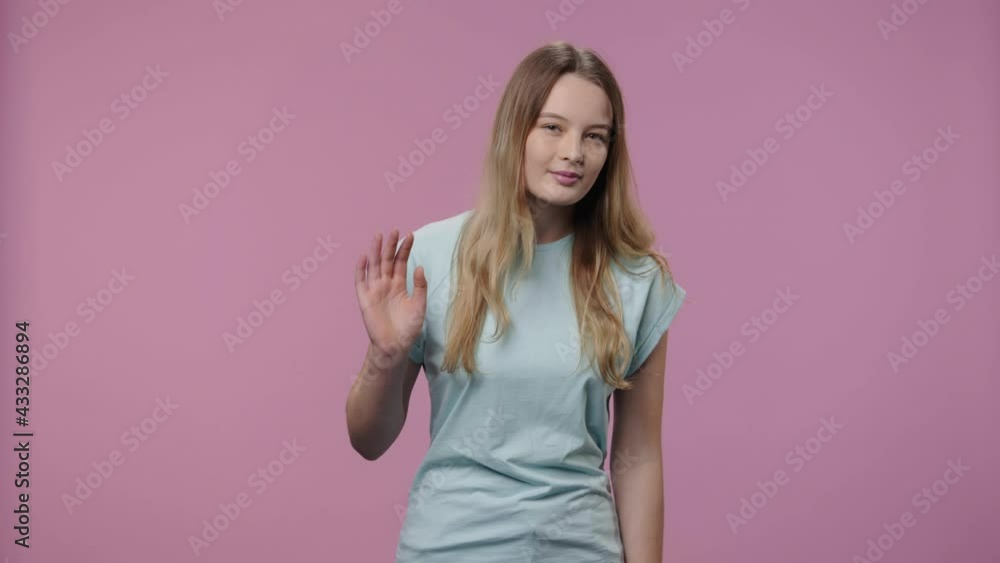 Portrait of model with natural beauty waves hello and makes hand gesture to come here. Young girl with long hair in blue t-shirt poses on purple studio background. Close up. Slow motion ready 59.94fps Portrait of model with natural beauty waves hello and makes hand gesture to come here. Young girl with long hair in blue t-shirt poses on purple studio background. Close up. Slow motion ready 59.94fps