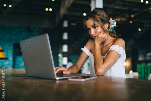 Upset woman working on laptop in cafeteria