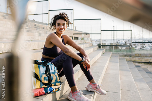Smiling sportsperson day dreaming while sitting by bag on staircase photo