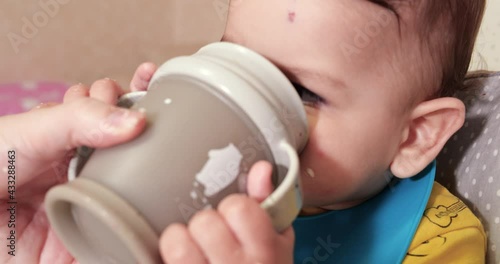 Cute baby boy drinking a glass of water at home. Close-up. The child drinks water from a plastic sippy cup