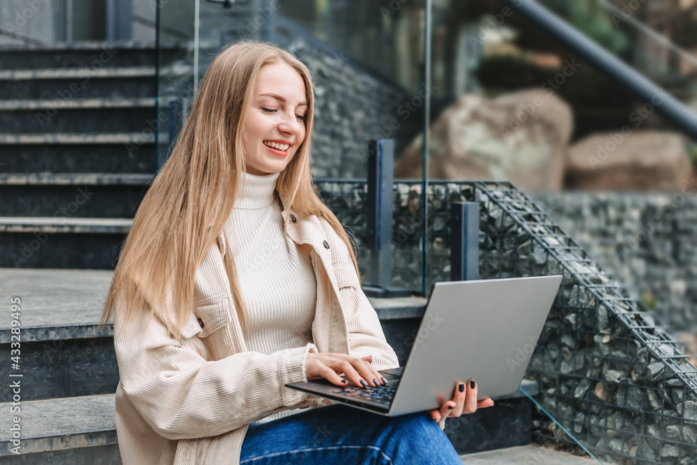 Happy student girl sitting on stairs near office center with laptop smiling and studying. online education Happy student girl sitting on stairs near office center with laptop smiling and studying. online education