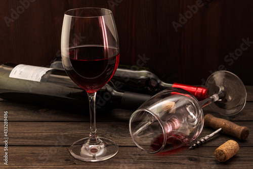 Two bottles of red wine with two glasses and corkscrew with cork on an old wooden table. Focus on an overturned glass of wine