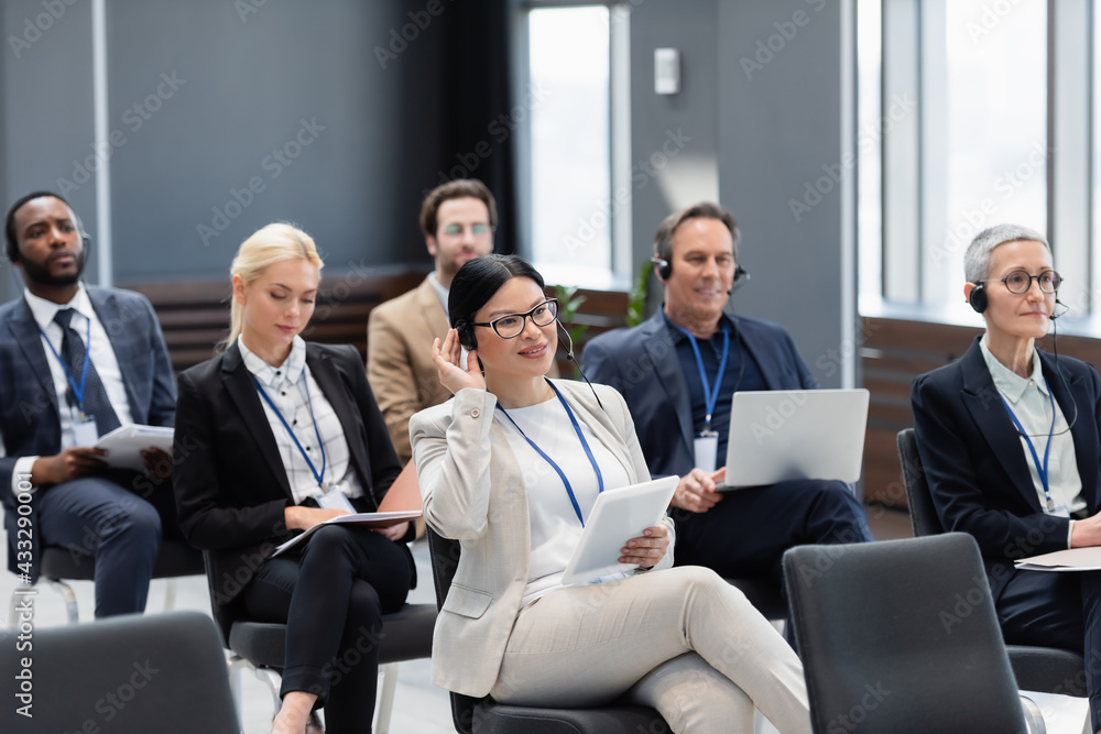 Smiling asian businesswoman in headset holding digital tablet during seminar Smiling asian businesswoman in headset holding digital tablet during seminar