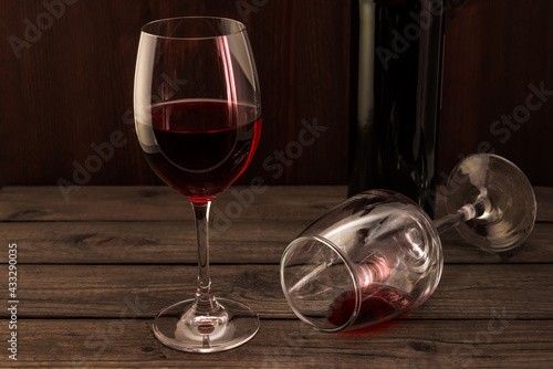 Bottle of red wine with two glasses on an old wooden table. Focus on an overturned glass of wine photo