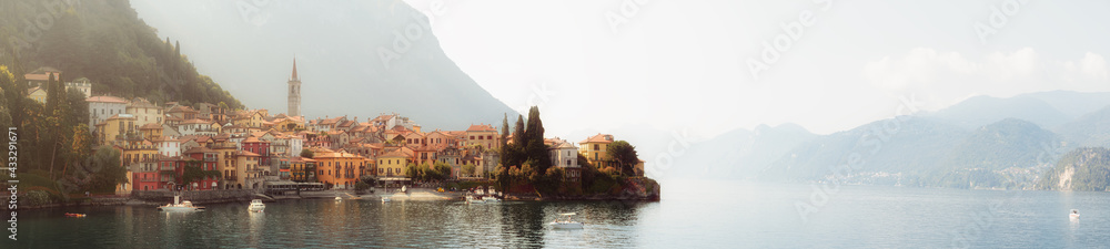 Early morning view of the Como Lake with the village of Varenna, Italy, and clear sky, with fog, soft sunlight and mountains in the distance