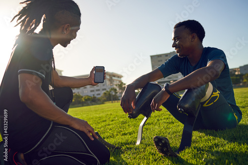 Coach with smart phone talking to amputee athlete in sunny grass