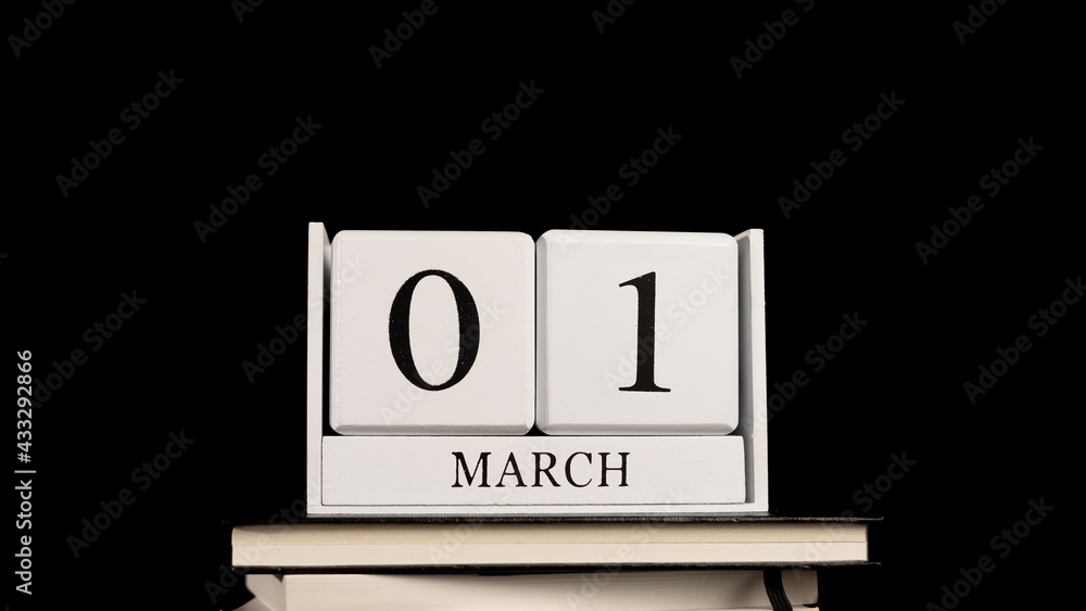 Cube wooden calendar on a pile of books, on first day of March with black background. Cube wooden calendar on a pile of books, on first day of March with black background.