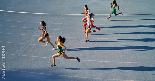 Female track and field athletes running in competition on blue track photo