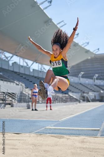 Female track and field athlete long jumping over sand photo