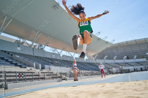 Female track and field athlete long jumping over sand
