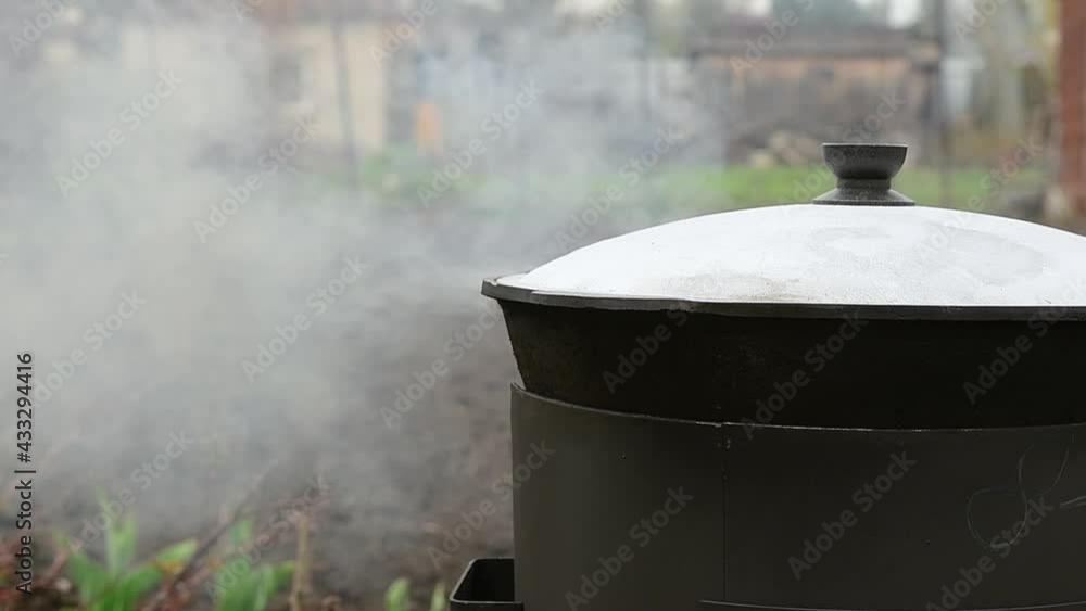 Food is prepared in a cauldron outdoors in the courtyard. Boiling water vapor. Slow motion. The man opens the lid of the pan. Two videos. Food is prepared in a cauldron outdoors in the courtyard. Boiling water vapor. Slow motion. The man opens the lid of the pan. Two videos.