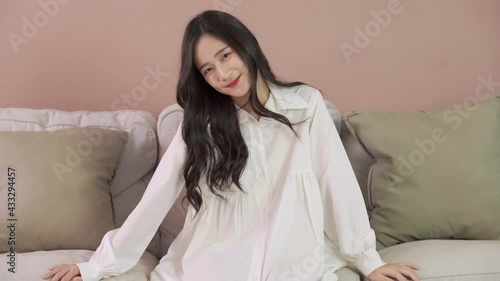 Cute Asian girl in white dress sit on sofa and smile
