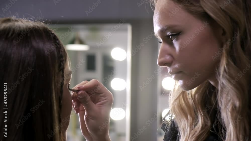 professional visagiste working at salon, preparing pretty woman for event, photoshoot. applying rhinestones to eyelid of beautiful young brunette female model with tweezers. beauty industry, self-care professional visagiste working at salon, preparing pretty woman for event, photoshoot. applying rhinestones to eyelid of beautiful young brunette female model with tweezers. beauty industry, self-care
