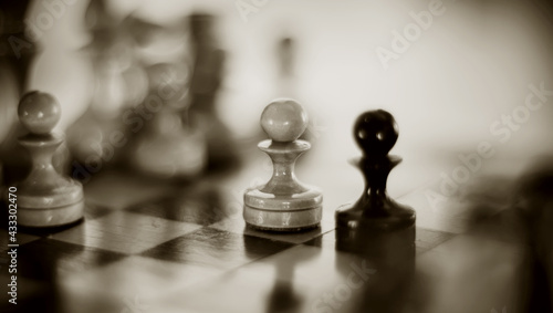 Two chess pieces are pawns: black and white. Wooden chess pieces on the chessboard.