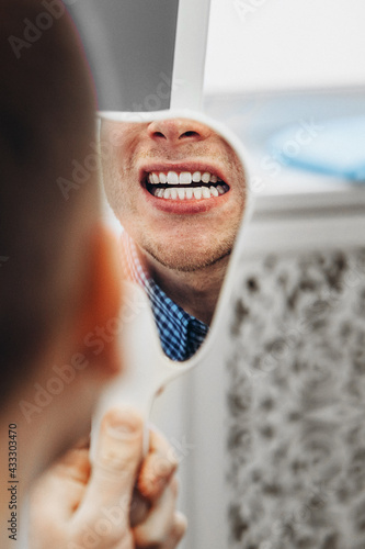 Man is looking at mirror and enjoying reflectiong of his smile after dental procedures. photo