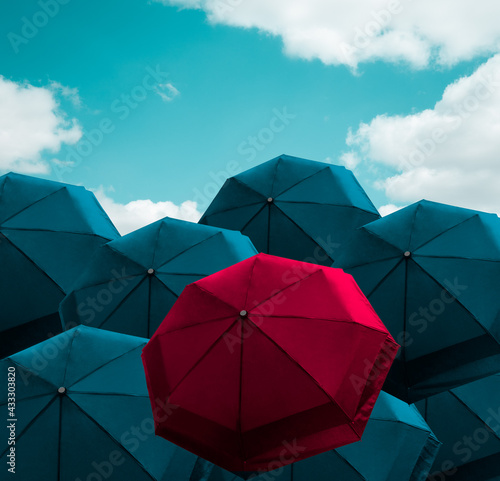 Prominent vivid red umbrella among group of blue parasol on cloudy blue sky  protection item for sunny and rainy weather. Protective idea with repetition pattern. Differentiate  outstanding concept.