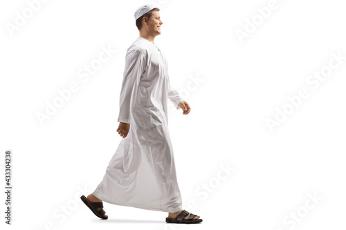 Full length profile shot of a young muslim man in white dishdasha walking