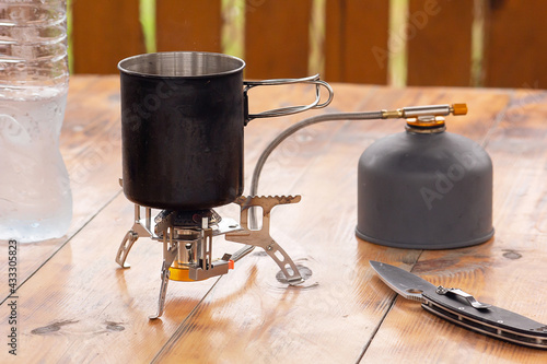 a metal mug stands on a camping gas stove, next to a propane tank