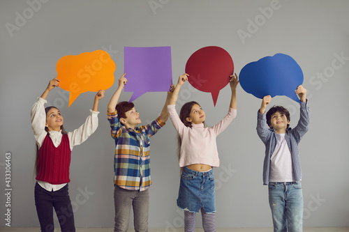 Children of new generation express opinions. Group of cute junior kids holding up multicolored clean paper bubbles. Happy smiling elementary school boys and girls with text bubbles standing in studio