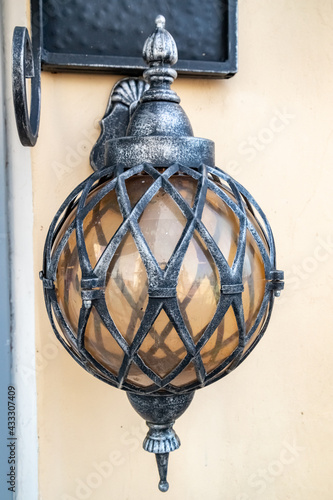 Wall-mounted round forged street lamp in an elegant metal braid.