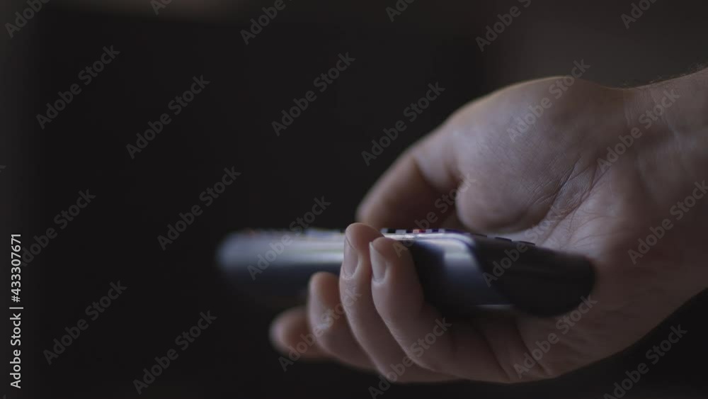 Man watches smart TV and uses black remote control. Person controls TV using a modern remote control Man watches smart TV and uses black remote control. Person controls TV using a modern remote control