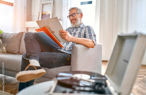 A mature man sits on the couch at home, relaxes, enjoys life and listens to vinyl records on a music player.Turntable playing vinyl LP record.