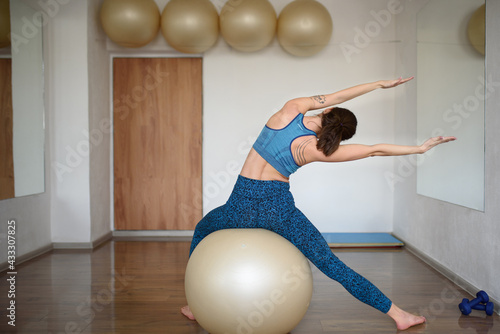 A young athletic woman sits on fitball and does side bends in the gym.Pilates