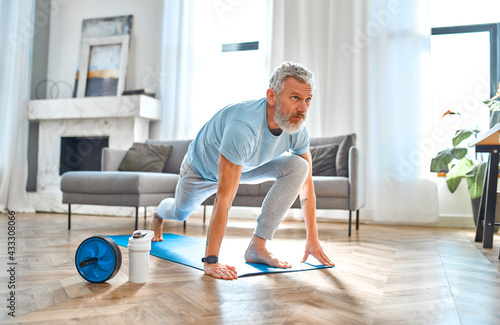Fototapeta Naklejka Na Ścianę i Meble -  Sport, fitness and healthy lifestyle concept. Mature man doing exercises at home. How to stay healthy on quarantine concept.